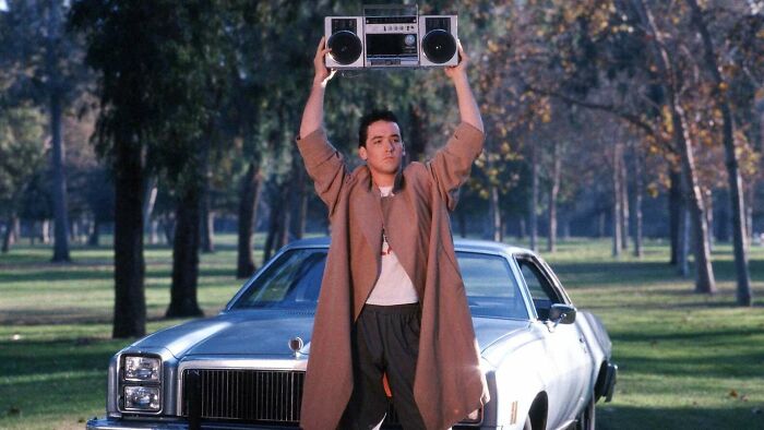 A person holds a boombox over their head in a classic scene from a park, illustrating famous movie props stories.