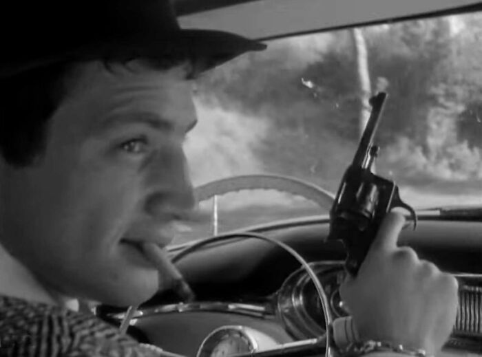 "Character holding a prop gun, driving with intense expression, illustrating famous movie props stories."