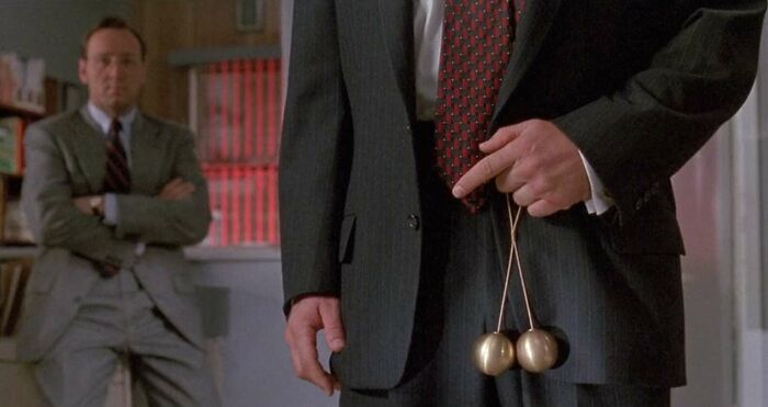 Man in a suit holding movie props with a colleague in the background.