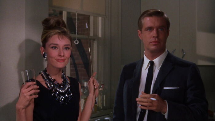 Two characters holding drinks, dressed elegantly, in a scene featuring famous movie props.