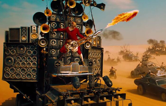 Flamethrower guitar from a famous movie prop scene in a desert battle with vehicles and speakers.