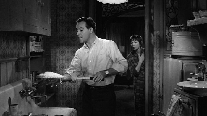 Man cleaning a dish in a vintage kitchen with a woman observing, illustrating famous movie props stories.