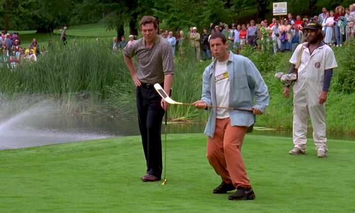Man on golf course with hockey stick, iconic movie prop surrounded by onlookers.