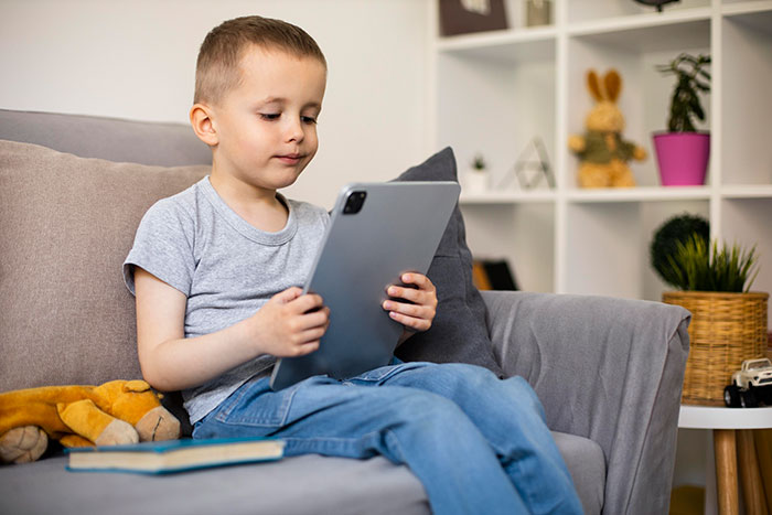 Young child using an iPad on a couch, illustrating the concept of an "iPad kid" in a modern living room setting. Young child using an iPad on a couch, illustrating the concept of an "iPad kid" in a modern living room setting.
