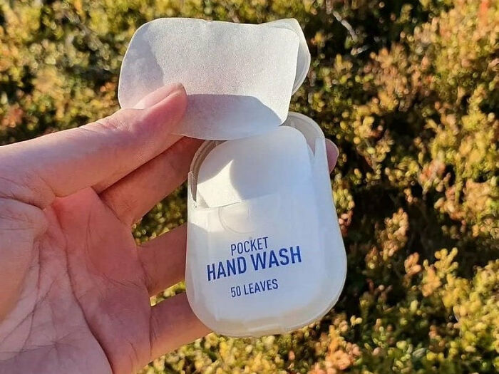 Pocket hand wash with 50 leaves, a travel essential, held up against a leafy background.