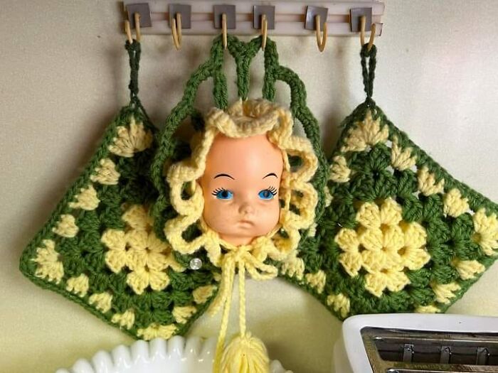 Horrendous DIY project: a doll head incorporated into yellow and green crochet kitchen decor.