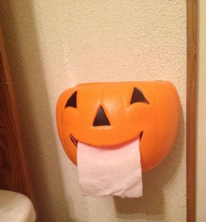 Pumpkin face wall decor dispensing toilet paper in a humorous DIY project.