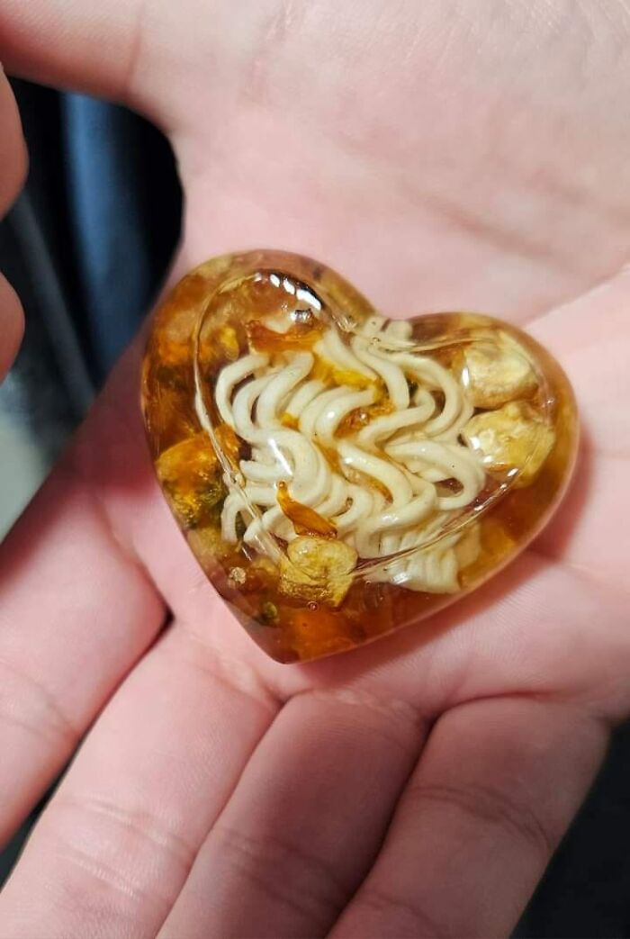 Heart-shaped resin craft encasing noodles, held in a hand, exemplifying horrendous DIY projects.
