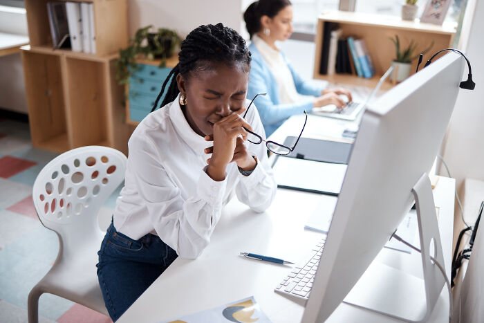 Frustrated woman at desk holding glasses with eyes closed, capturing a real moment of insane workplace stress and tension.