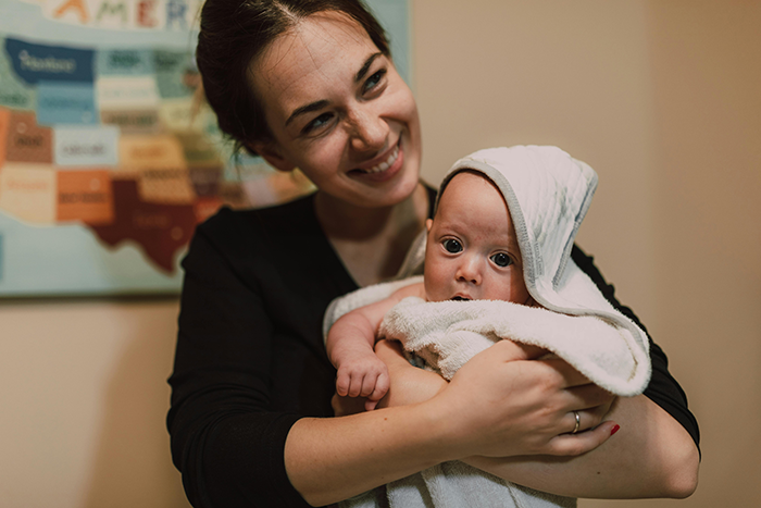 Woman holding a baby in a towel, smiling warmly in a cozy room with a map on the wall.
