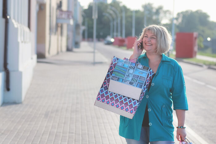 A woman walking outdoors with a shopping bag, smiling and talking on the phone. A woman walking outdoors with a shopping bag, smiling and talking on the phone.