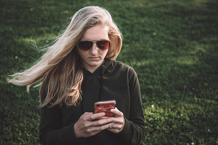 Woman in sunglasses looking at her phone, standing on grass, related to ungrateful sibling situation. Woman in sunglasses looking at her phone, standing on grass, related to ungrateful sibling situation.