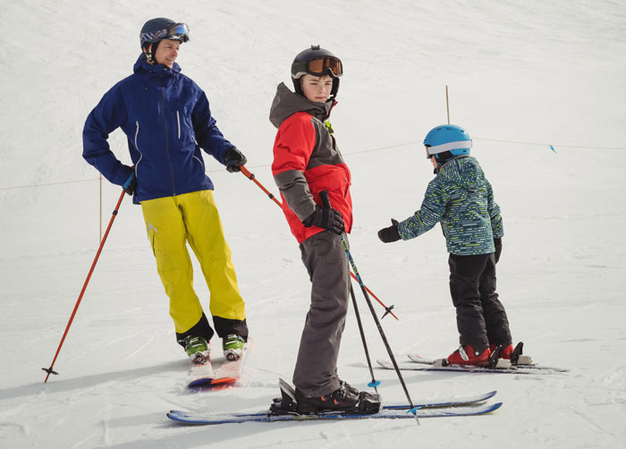 Adult skier with two kids on beginner trail.