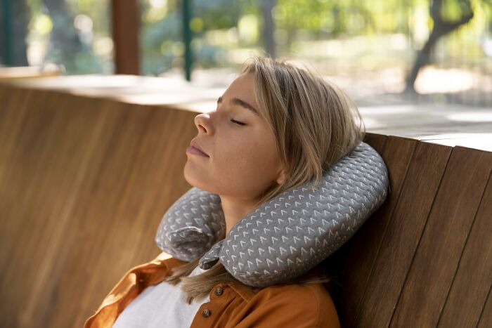 Woman using a travel neck pillow, resting peacefully on a wooden bench, illustrating game-changing travel essentials.