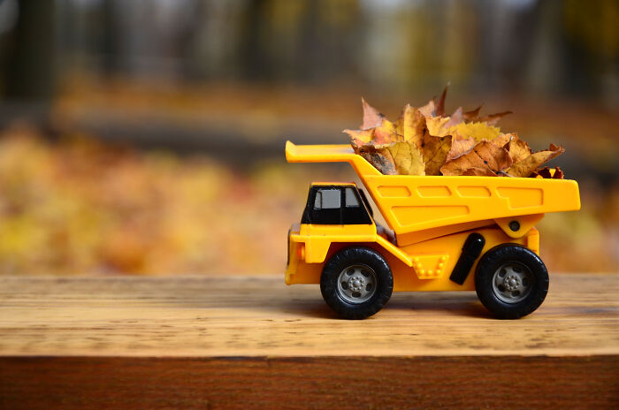 Toy dump truck carrying autumn leaves on a wooden surface, highlighting potential price hikes in goods and services.