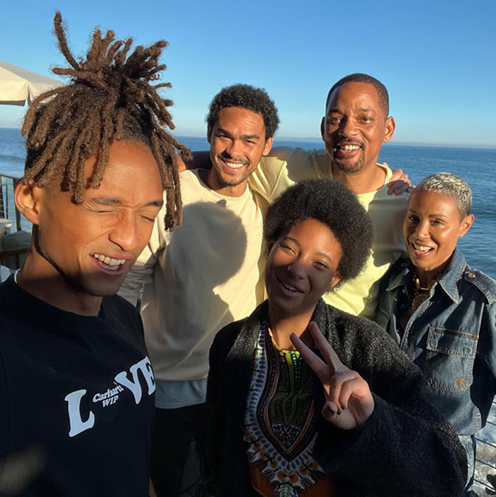 Family enjoying a sunny day by the ocean, smiling and posing for a group photo.