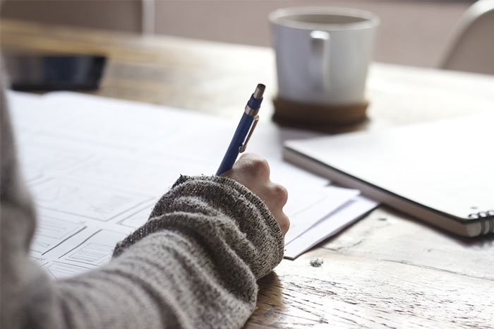 Person writing notes at a wooden desk with coffee mug, focusing on critical things to know.