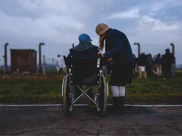 Person assisting someone in a wheelchair outdoors, highlighting critical knowledge of accessibility and empathy.