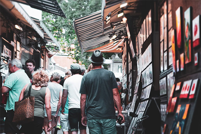 People walking through a bustling street market, surrounded by art displays and shops, in an urban setting.