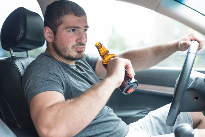Man in a gray shirt drinking from a bottle while driving, highlighting critical safety awareness issues.