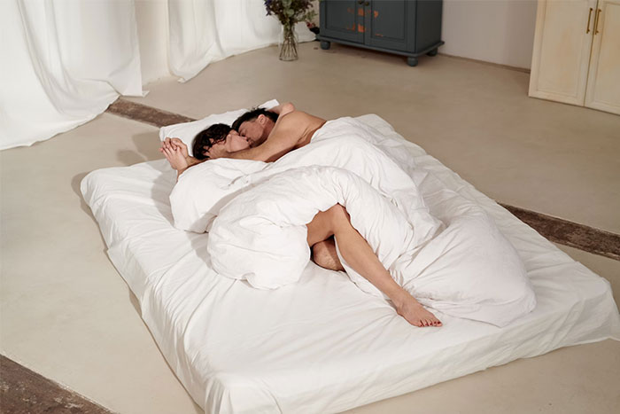 Couple sleeping on a white bed, wrapped in blankets, highlighting essential sleeping practices.