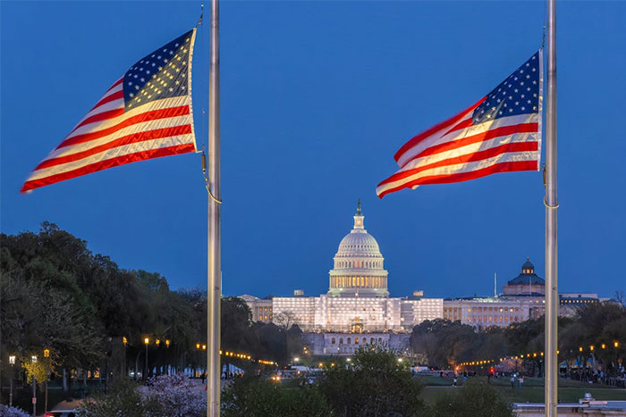 U.S. Capitol building illuminated at night with two American flags, symbolizing critical knowledge landmarks.