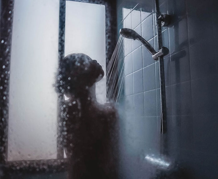 Person showering behind a foggy glass door, demonstrating critical daily routines.
