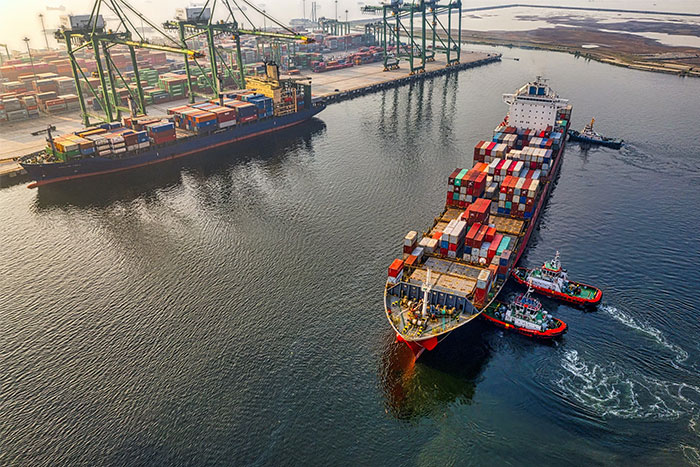 Cargo ship in a busy port, loaded with colorful containers, maneuvered by tugboats, showcasing global trade logistics.