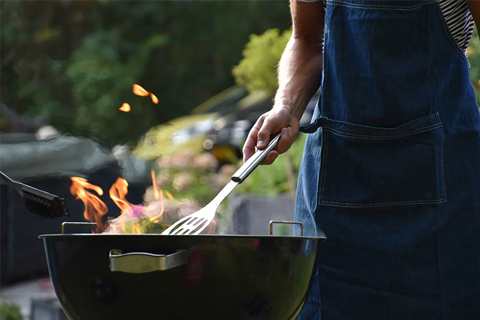 Person grilling outdoors, wearing a denim apron, managing flames with a spatula.