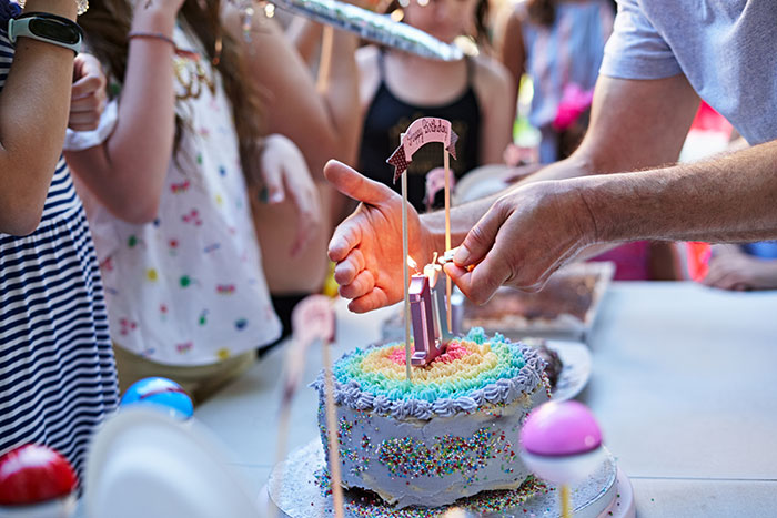 Birthday cake being decorated at a child's party, surrounded by children.
