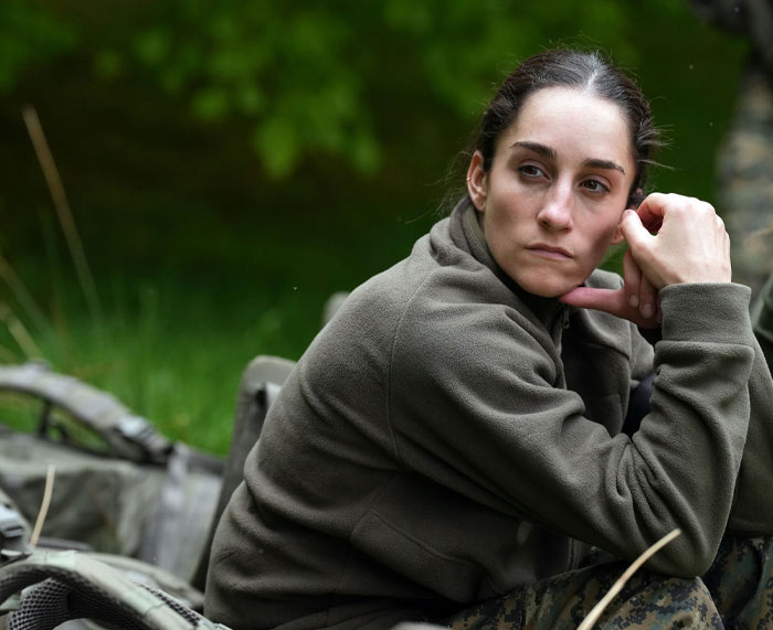 Jordyn Wieber of Special Forces Season 3 sitting outdoors, wearing a green jacket, contemplating in a military setting.
