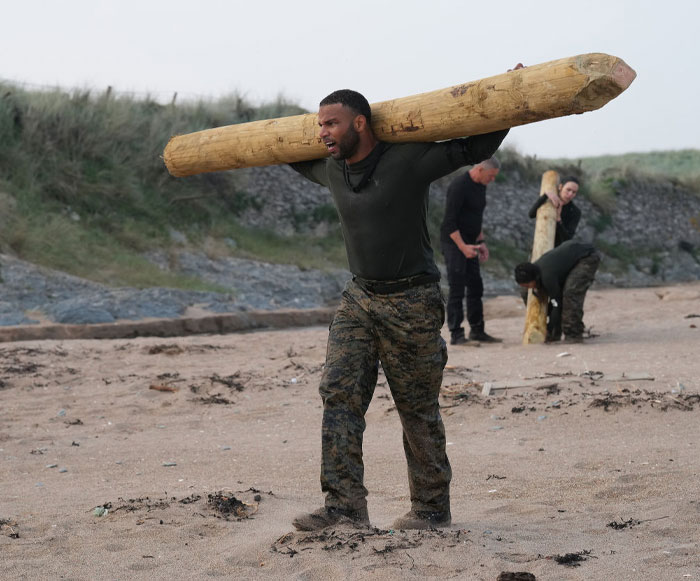 Golden Tate training on a beach for Special Forces Season 3, lifting wooden logs as part of a survival challenge.