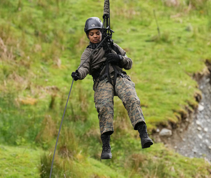 Kyla Pratt rappelling in military gear during Special Forces training on a grassy terrain.