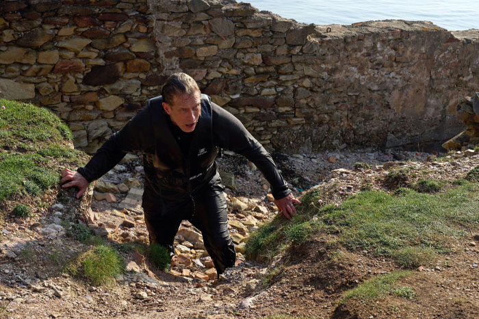 Stephen Baldwin climbing rocky terrain during Special Forces training challenge.