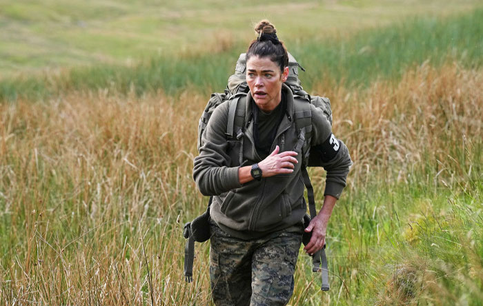 Denise Richards trekking with backpack in a grassy field, part of Special Forces Season 3 cast enduring challenges.