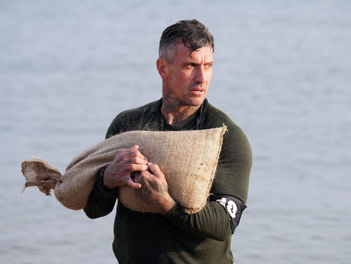 Special Forces participant Carey Hart carrying a sandbag on a beach, showcasing endurance during the toughest test.