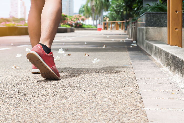 Person walking on a sidewalk wearing red sneakers surrounded by litter, relating to disgusting everyday habits.