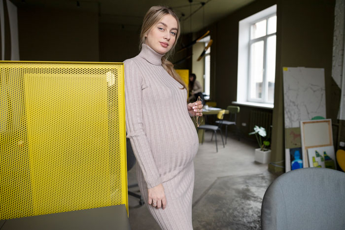 Pregnant teenager indoors, continuing family legacy, wearing beige dress, in modern room with yellow accents.