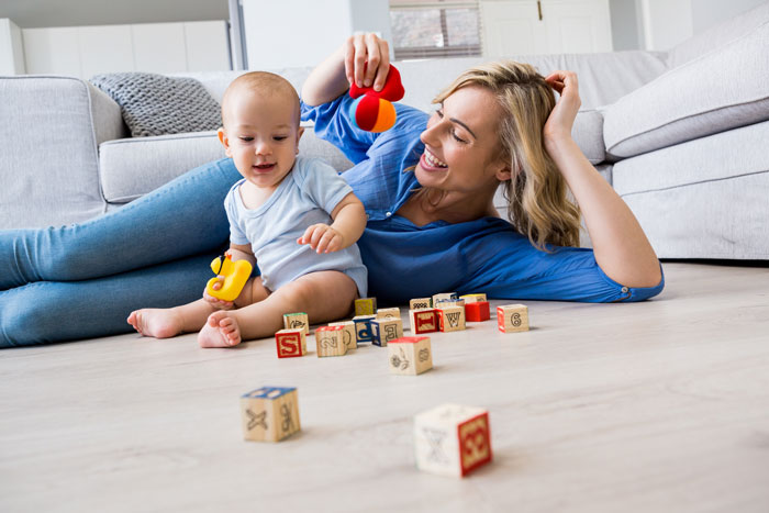 Woman babysitting, playing with a baby on the floor, surrounded by colorful blocks.