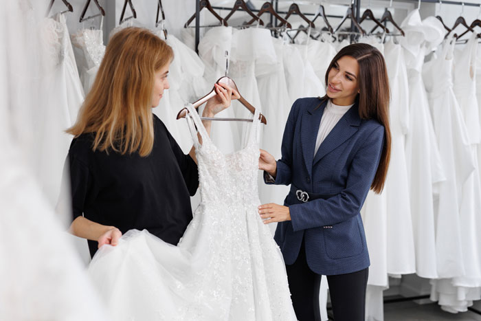 Women dress shopping, analyzing a wedding gown among several, aligned with dad choosing wife over daughter situation.
