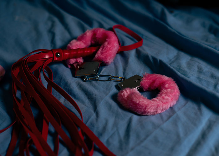 Fuzzy pink handcuffs and red whip on a blue sheet, representing strange hotel room discovery by housekeepers.