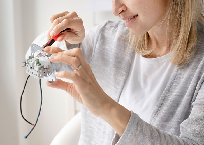 A woman fixing a light switch with a screwdriver, focusing intently, in a well-lit room.