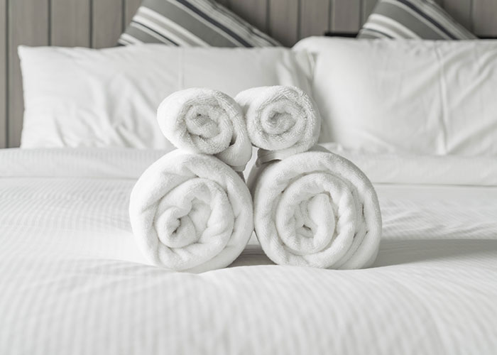 Rolled towels resembling a sculpture on a hotel bed, in a neatly arranged room setting.