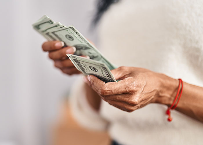 A person counting a stack of US dollars, highlighting hotel housekeepers' discoveries in rooms.