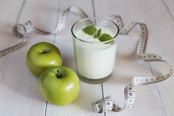 Glass of yogurt with green apples and measuring tape, symbolizing corporate propaganda influences on health perceptions.