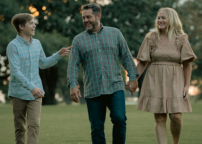 A man and woman holding hands with a laughter-filled boy, enjoying a walk in the park, representing family dynamics and boundaries.