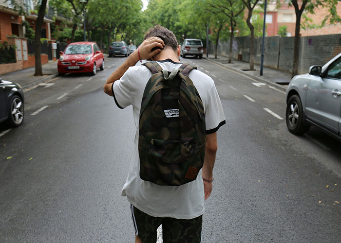 Young man wearing a backpack walks on a tree-lined street, illustrating a nephew cared for by his uncle.