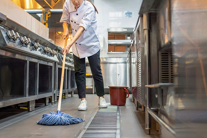 Chef mopping the restaurant kitchen floor, highlighting cleanliness issues in a bad restaurant.