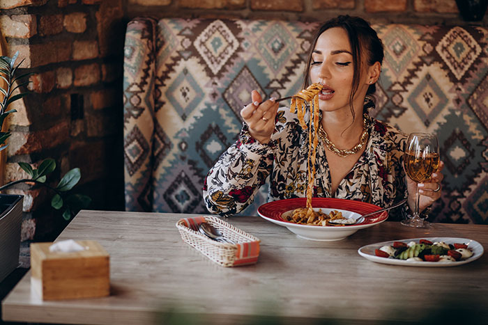 Woman dining alone in a restaurant with pasta and wine, showing signs of a bad restaurant experience.