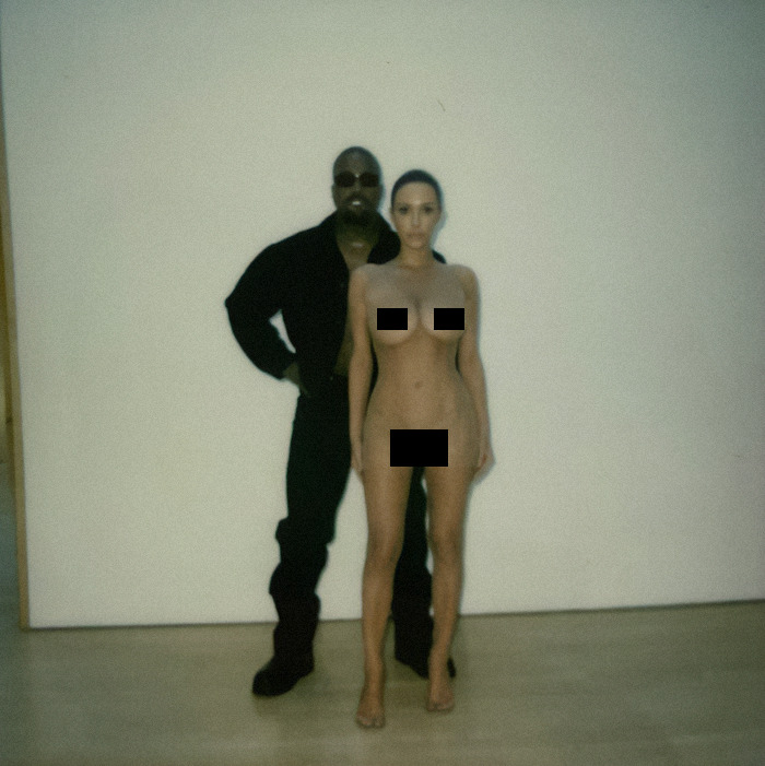 Bianca Censori and Kanye West posing for a photo in front of a plain wall indoors.